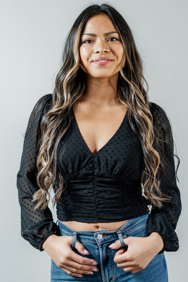 Pictured is a black, peasant-style top with a v-neckline, sheer balloon sleeves, and a cropped body.
