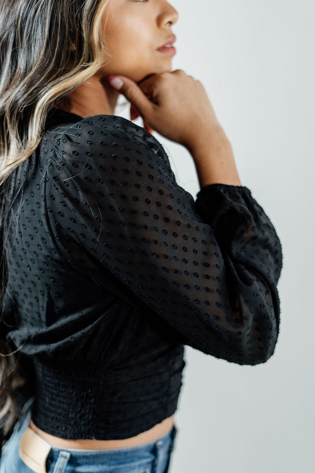 Pictured is a black, peasant-style top with a v-neckline, sheer balloon sleeves, and a cropped body.