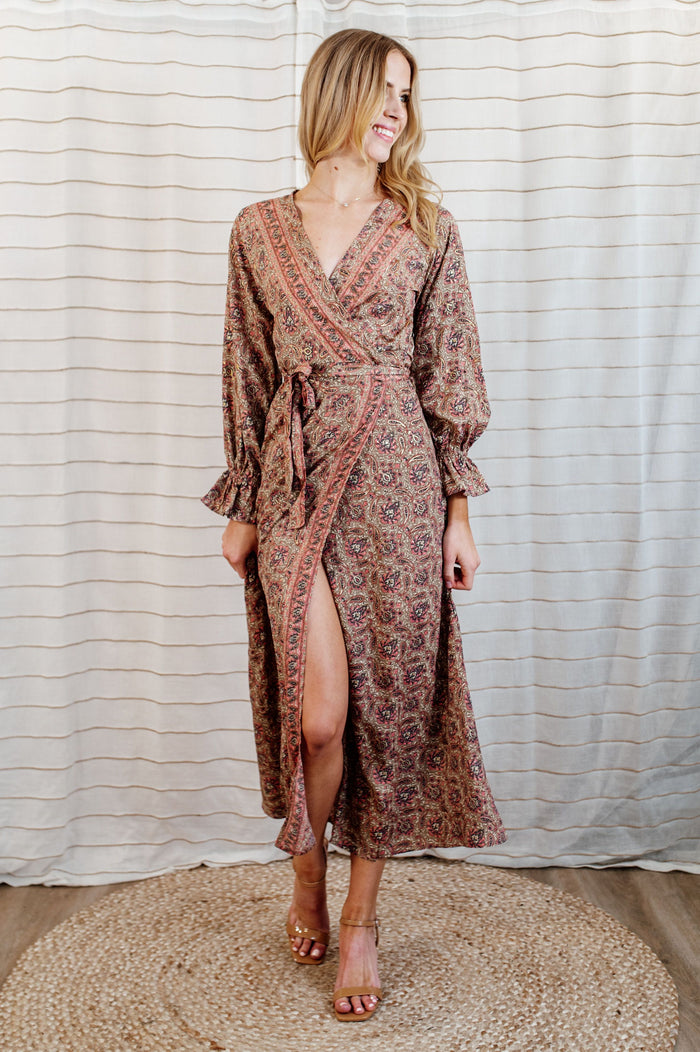 Pictured is a burgundy-clay, wrap maxi dress with a plunging v-neckline, ruffled flowy sleeves, and adjustable waist tie.