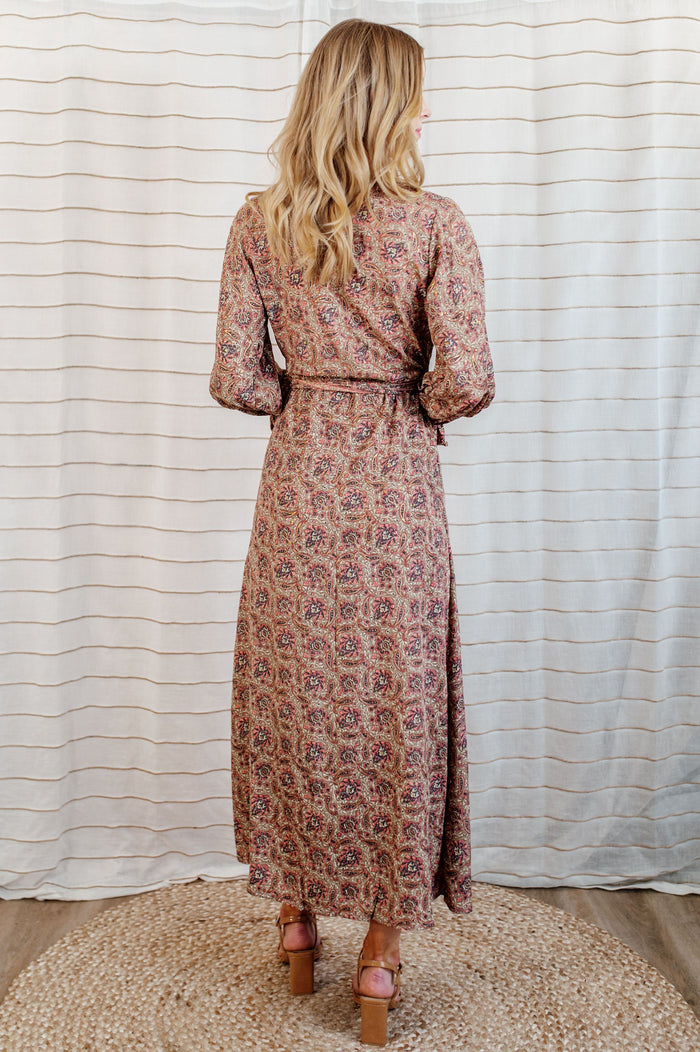 Pictured is a burgundy-clay, wrap maxi dress with a plunging v-neckline, ruffled flowy sleeves, and adjustable waist tie.