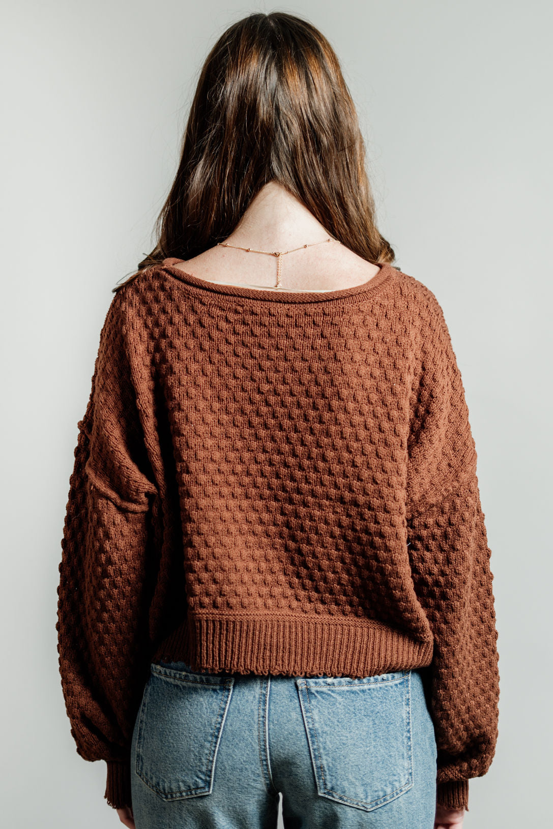 Pictured is a red-brown, knit sweater with a scoop neckline, cropped body, and cuffed knit sleeves.