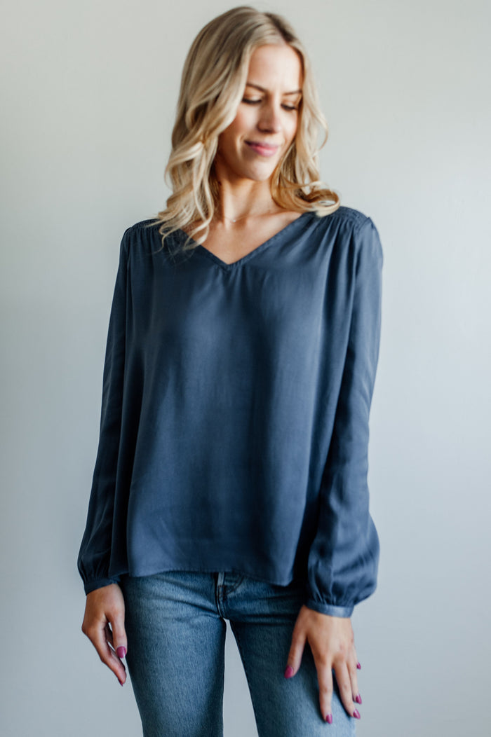 Pictured is a blue, flowy blouse with a v-neckline, balloon sleeves, and pleated back panel.