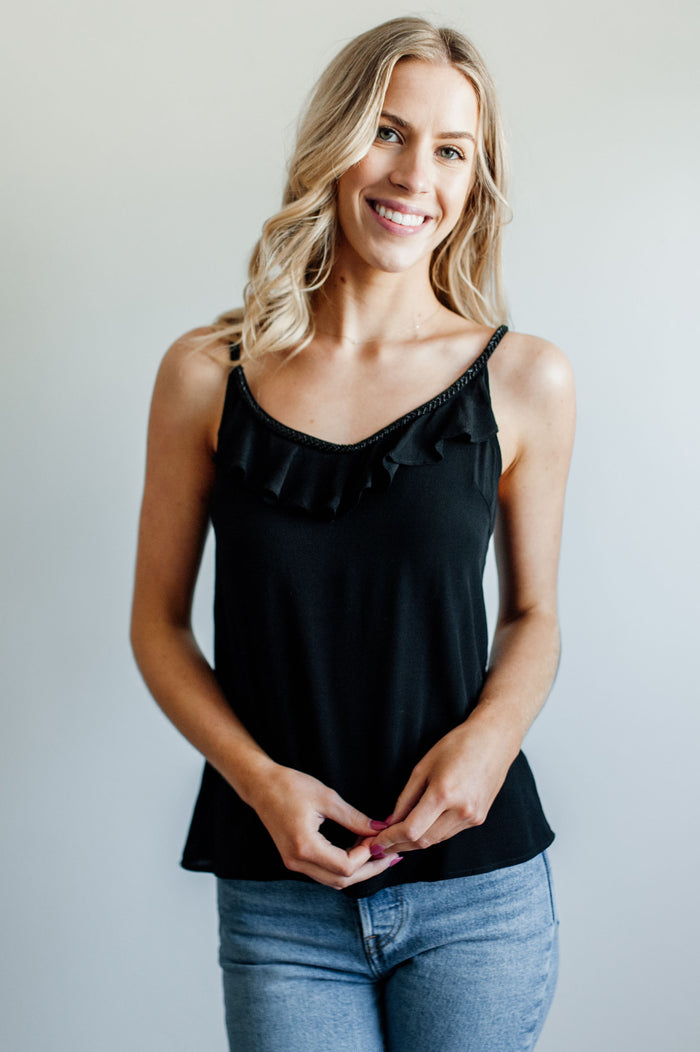 Pictured is a black, trendy top with beaded neckline, ruffle detailing, and tie back with tassels.