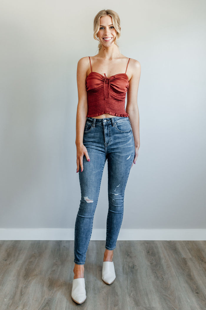 Pictured is a mid-wash, distressed denim jean with a high-rise waist, cropped ankles, and lightly distressed denim material.