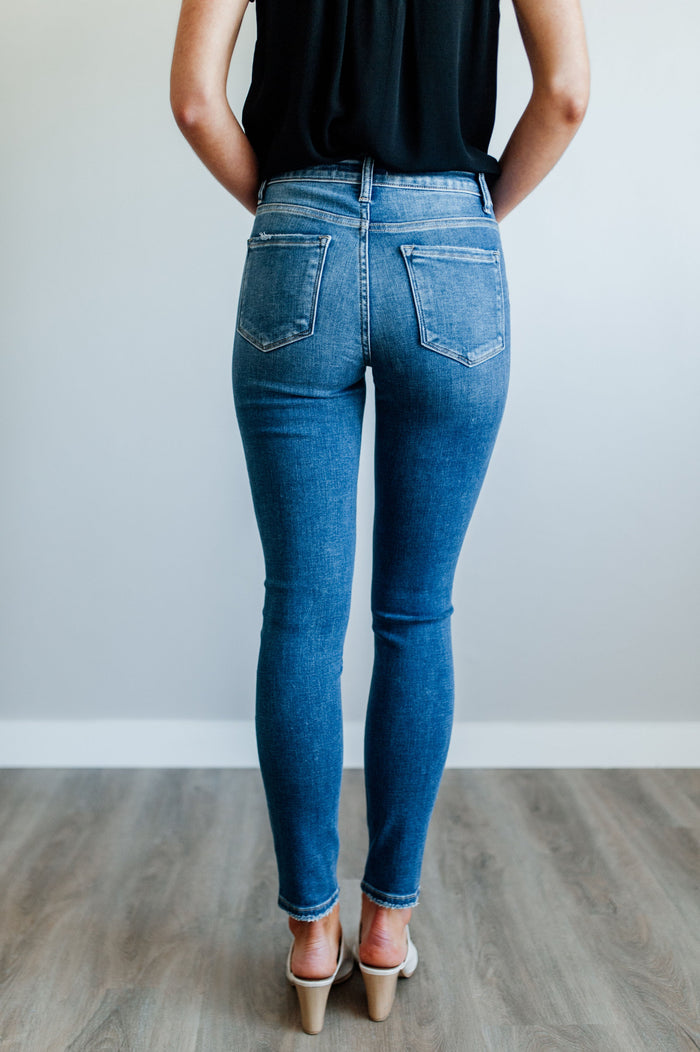 Pictured is a mid-wash, pair of denim with a mid-rise waist, medium-wash, knee slits, and cropped ankle with distressed hem.