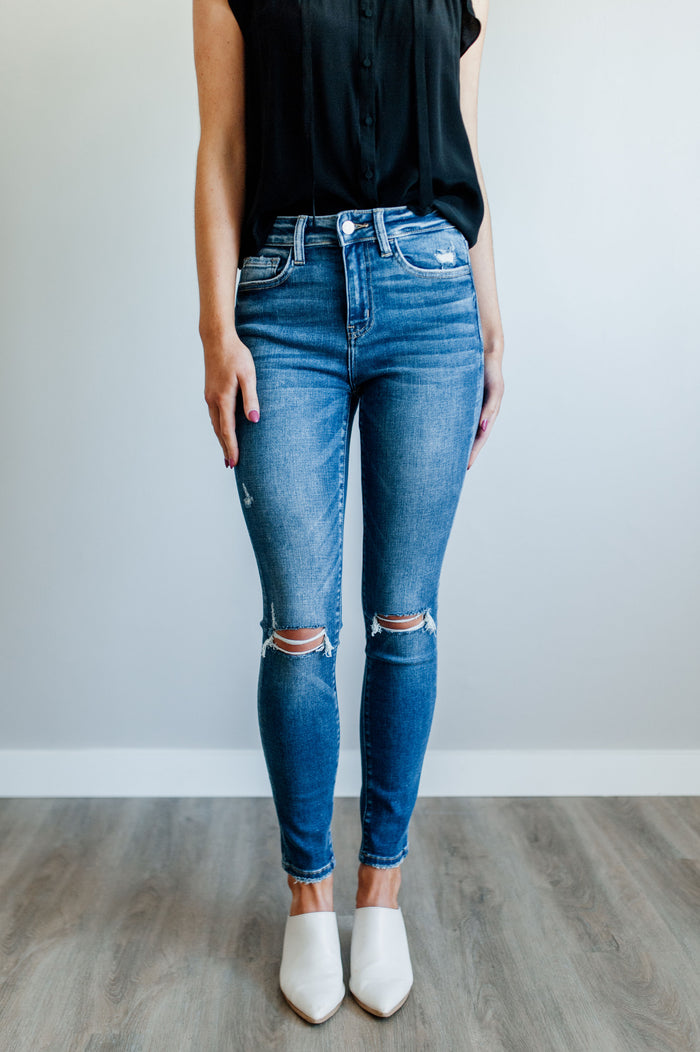 Pictured is a mid-wash, pair of denim with a mid-rise waist, medium-wash, knee slits, and cropped ankle with distressed hem.