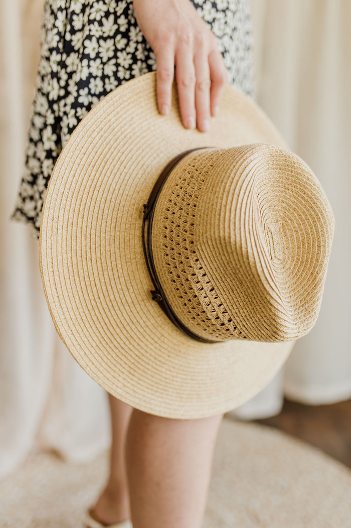 Pictured is a fedora-inspired sun hat comes in a tan color and features a fashionable brown leather-like band.