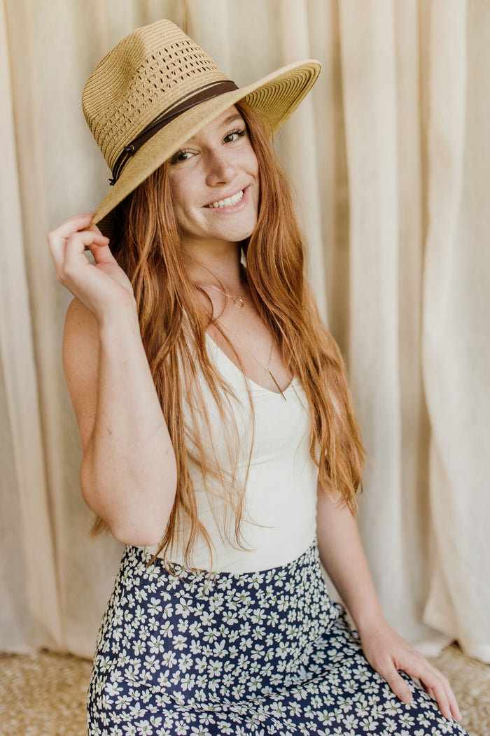 Pictured is a fedora-inspired sun hat comes in a tan color and features a fashionable brown leather-like band.