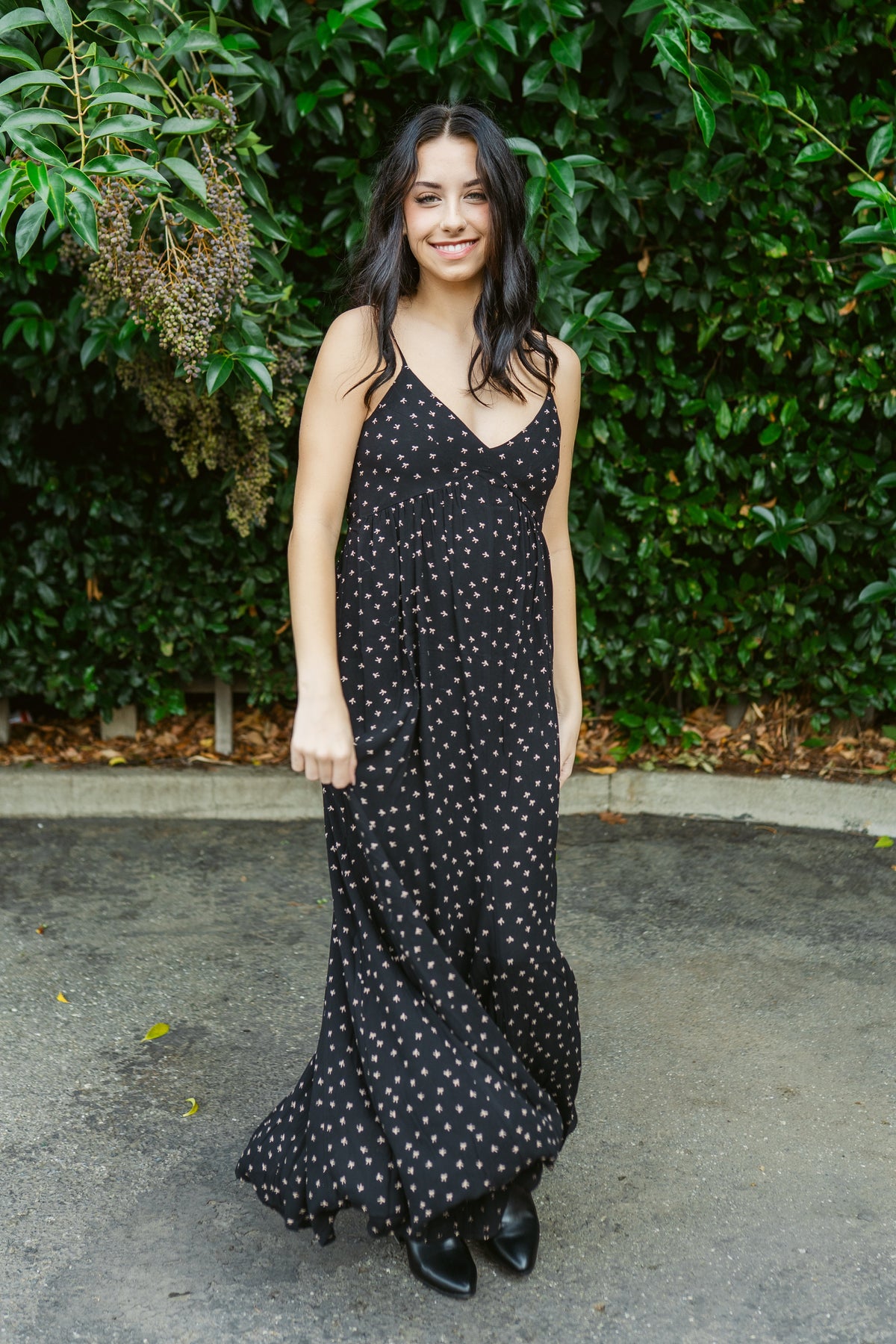 Woman wearing a black polka dot dress standing in front of green foliage.