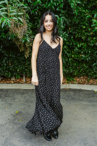 Woman wearing a black polka dot dress standing in front of green foliage.