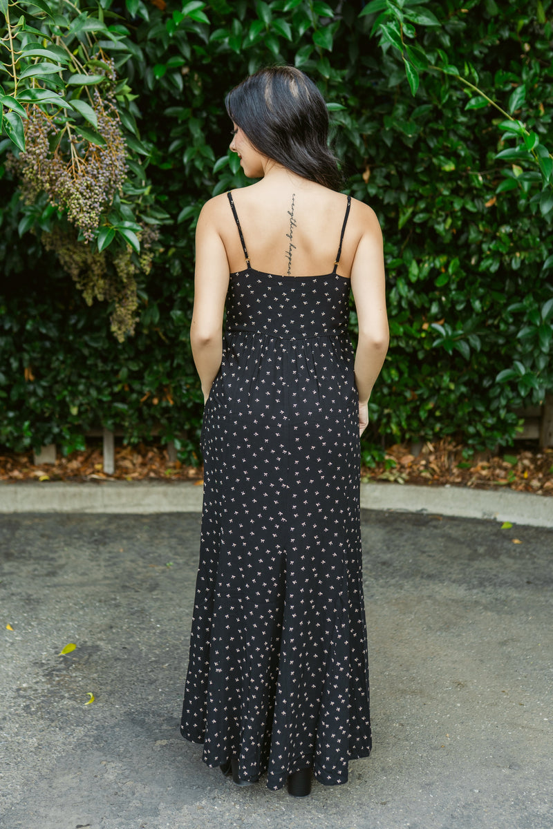 Woman wearing a black polka dot dress standing in front of green foliage.