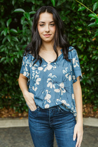 Woman wearing a blue floral blouse and jeans standing against a green leafy background