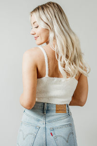 Pictured is a white, knit top with fuzzy material, thin shoulder straps, and cropped body. 