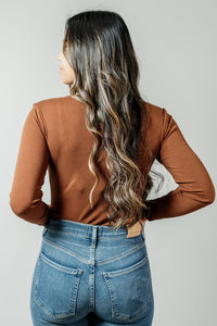 Pictured is a brown, long sleeve bodysuit with ribbed material. square neckline, and fitted body.