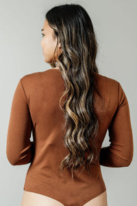 Pictured is a brown, long sleeve bodysuit with ribbed material. square neckline, and fitted body.