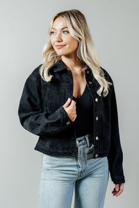 Pictured is a midnight-black denim jacket with a slightly cropped body, button-down front, and cuffed sleeves.