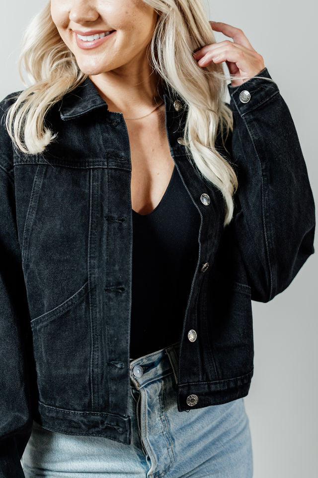 Pictured is a midnight-black denim jacket with a slightly cropped body, button-down front, and cuffed sleeves.