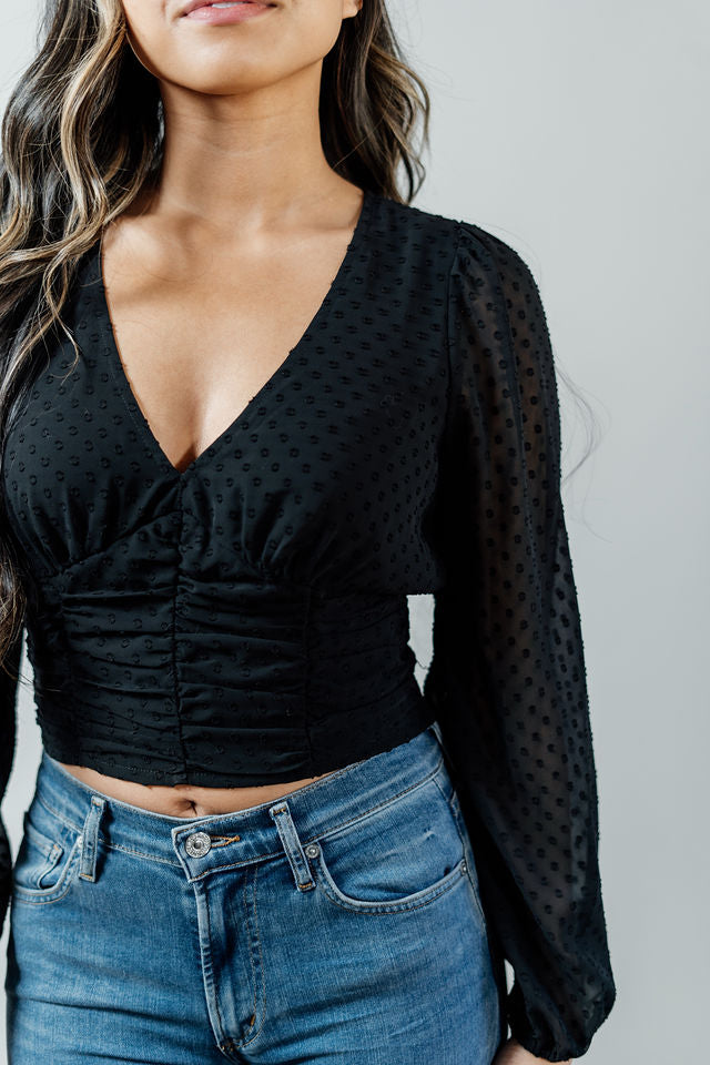 Pictured is a black, peasant-style top with a v-neckline, sheer balloon sleeves, and a cropped body.