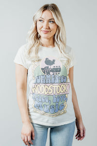 Pictured is a white graphic tee with pastel "Woodstock" branding and groovy detailing on a soft cotton material.