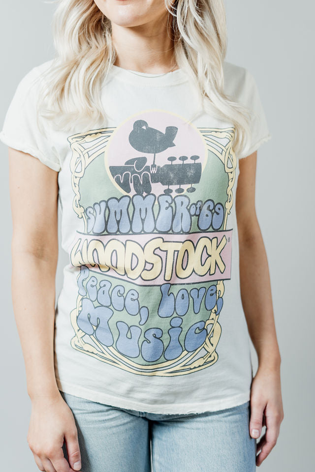 Pictured is a white graphic tee with pastel "Woodstock" branding and groovy detailing on a soft cotton material.