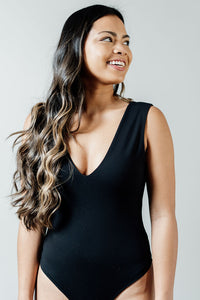 Pictured is a black bodysuit with a v-neckline,  double-lined material, thick shoulder straps, and two-button closure.