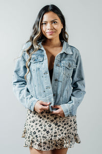 Pictured is a classic, blue denim jacket with a collar, button-down front, cuffed sleeves, and diamond detailing all over.