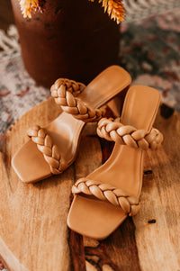 Pictured is a tan, heeled sandal with two braided straps and thin heel.