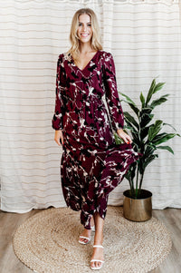 Pictured is a burgundy, long sleeve maxi dress with a lace trim v-neckline, puffed long sleeves, cinched waist, and side slit. 