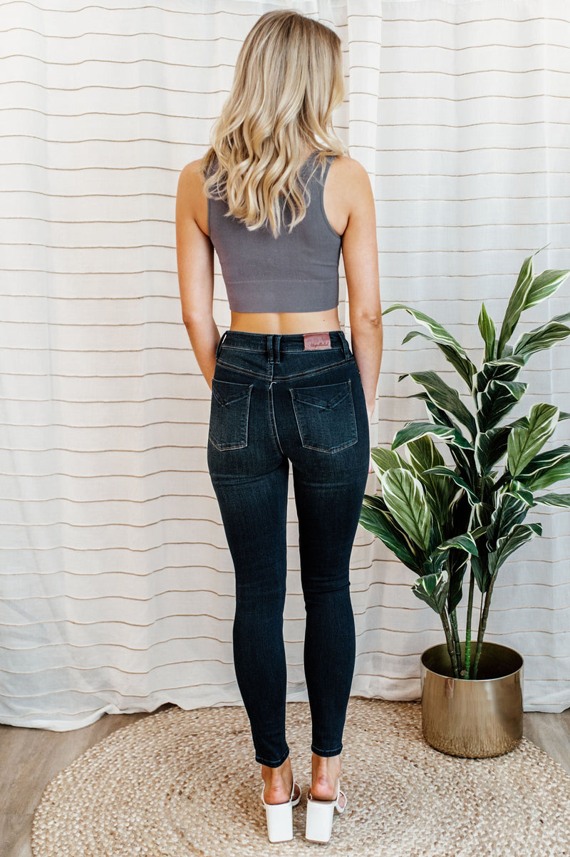Pictured is a pair of dark-wash denim with a button fly, a high-rise waist, cropped ankles, and dark wash denim material.