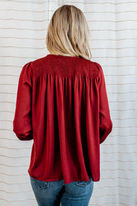 Pictured is a red, flowy blouse with a v-neckline, balloon sleeves, and pleated back panel.