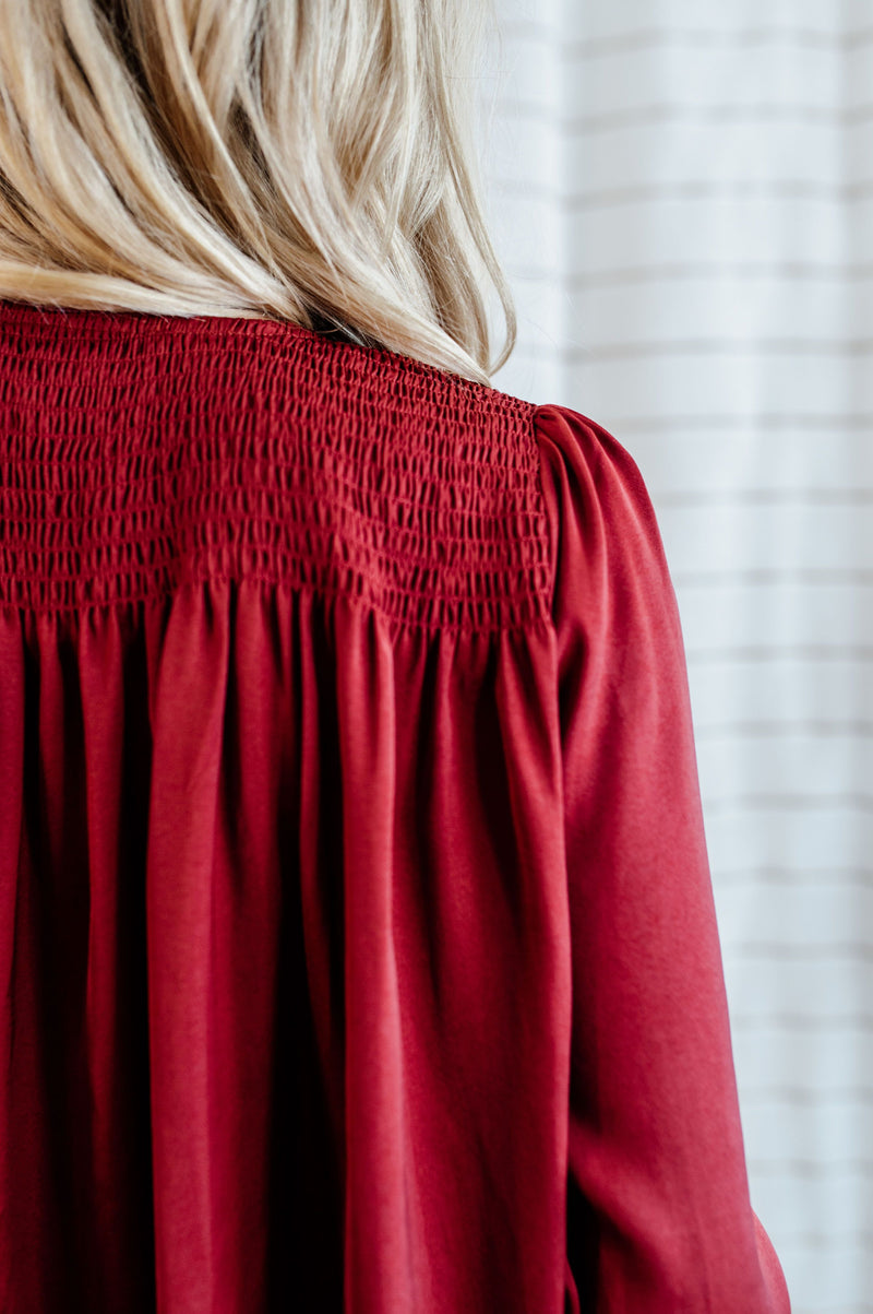 Pictured is a red, flowy blouse with a v-neckline, balloon sleeves, and pleated back panel.