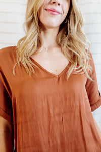 Peachy-orange colored blouse with cuffed sleeves and v-neck with flowy body on model.