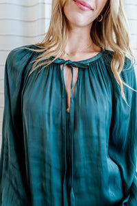 Teal blouse with flowy long sleeves and collar bow-tie on model.