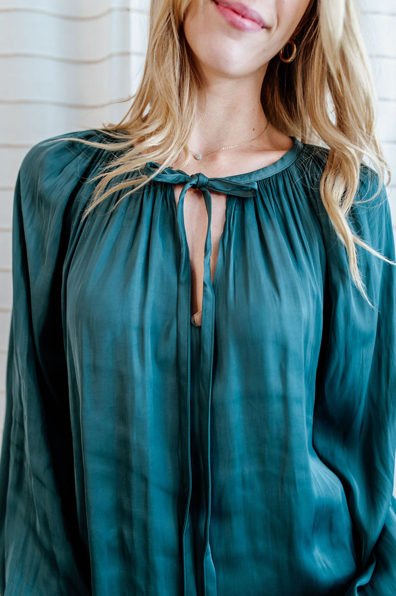 Teal blouse with flowy long sleeves and collar bow-tie on model.