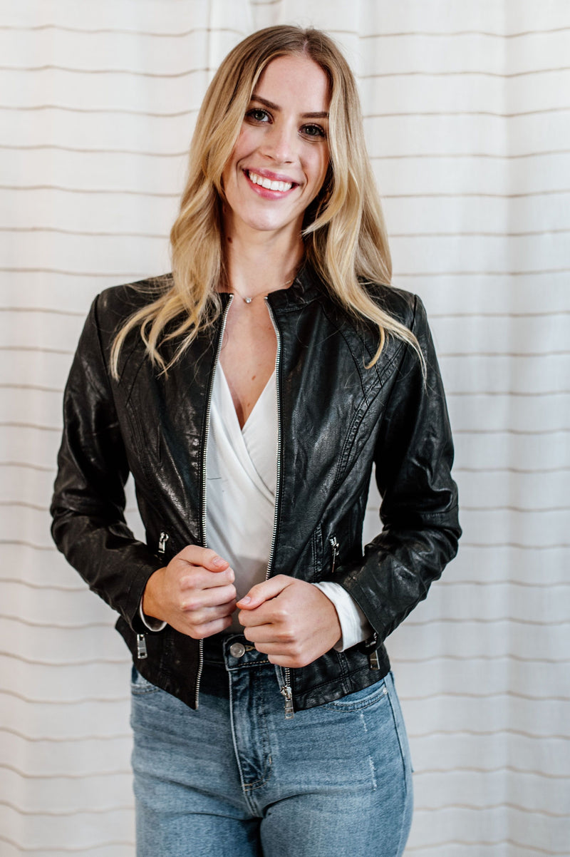 Pictured is a black, vegan faux leather jacket with an outside stitch detailing, floral-lined inside, and zipper detailing on the front, sleeves, and pockets.