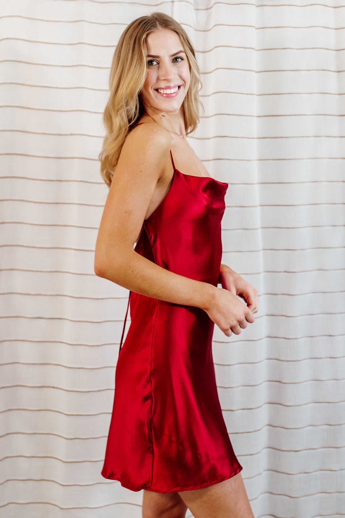Red, silky satin slip mini dress with cowl neck and flowy skirt on model.