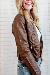 Pictured is a chocolate-brown, vegan faux leather jacket with an outside stitch detailing, floral-lined inside, and zipper detailing on the front, sleeves, and pockets.