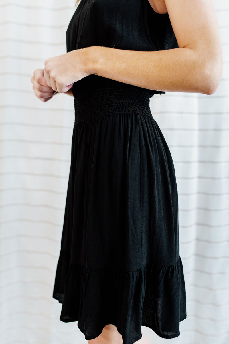 Black halter neck dress with elastic waist band and tiered skirt on model.