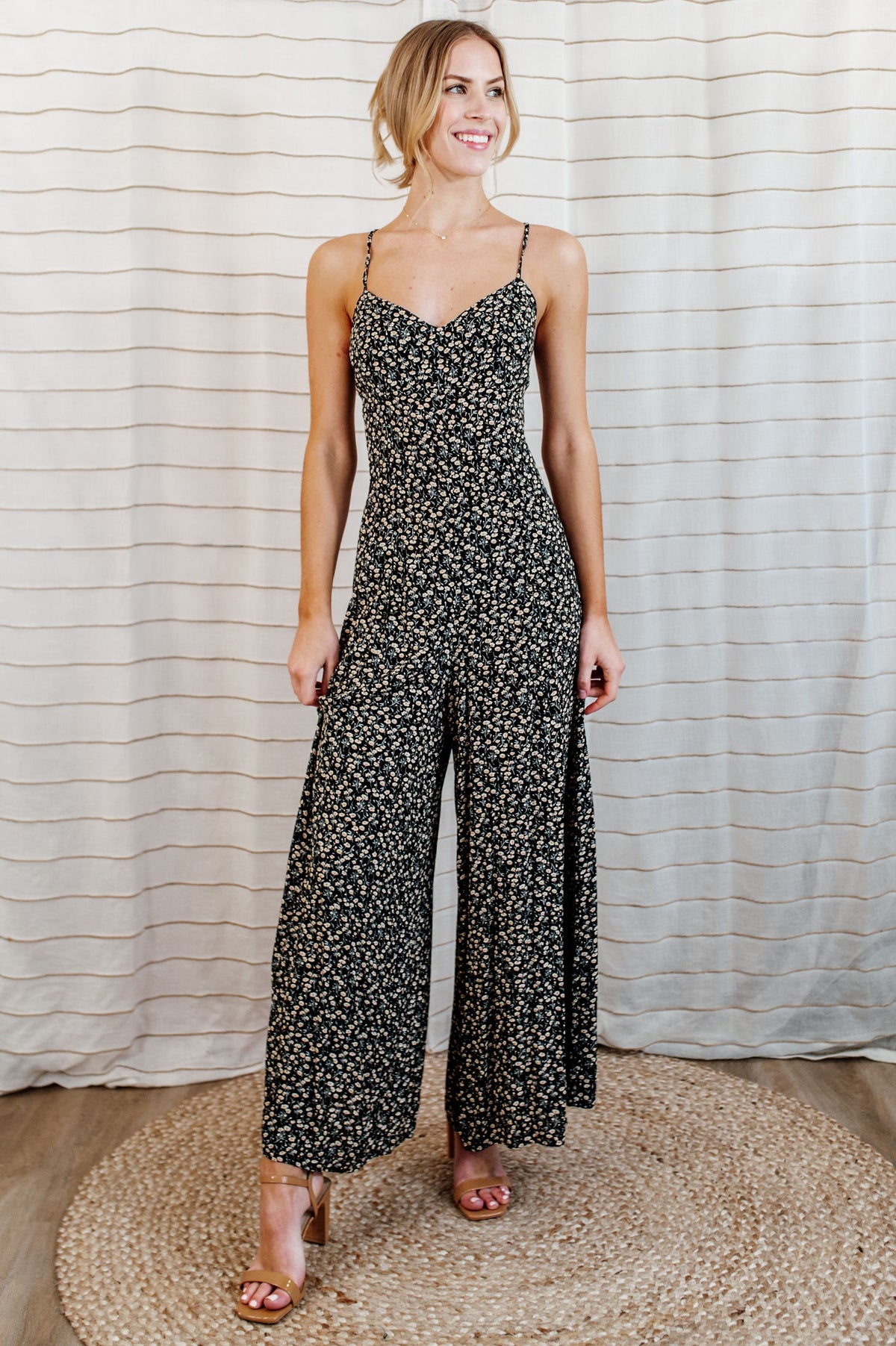 Pictured is a floral jumpsuit with a sweetheart bust, criss-cross shoulder ties, strappy open back, and wide-leg pants.