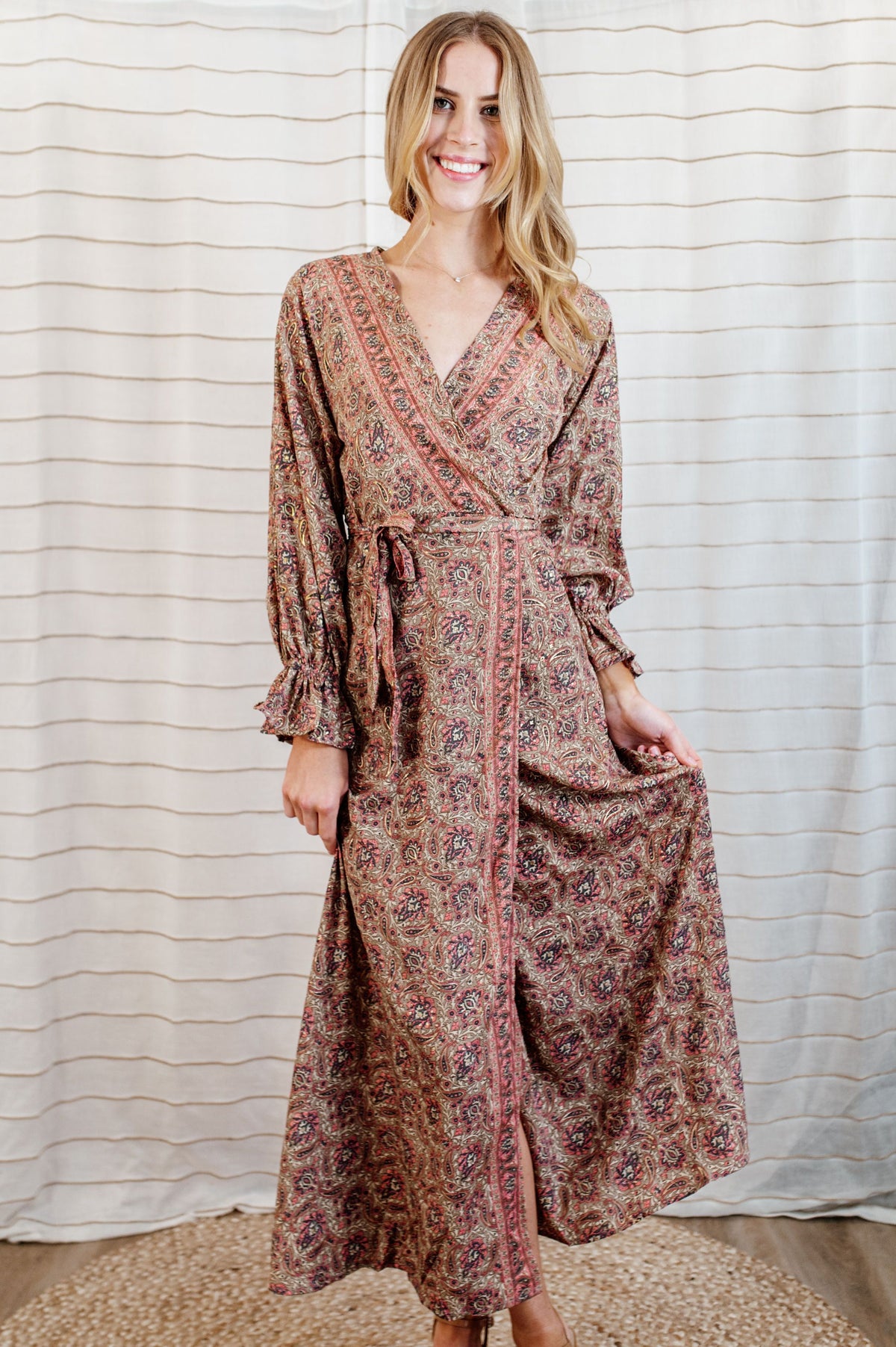 Pictured is a burgundy-clay, wrap maxi dress with a plunging v-neckline, ruffled flowy sleeves, and adjustable waist tie. 