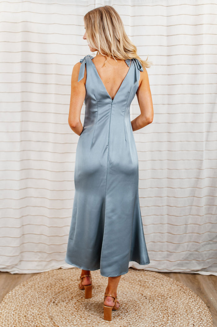 Pictured is a baby blue, silky midi dress with a v-neckline, large shoulder bow ties, and seamless back zipper.