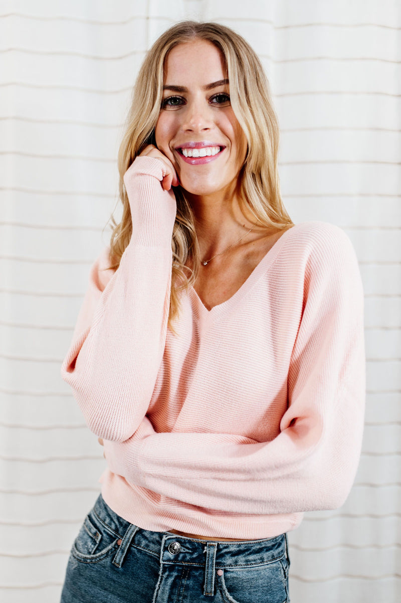 Pictured is a pink jersey pullover with a plush knit material, cuffed sleeves, cropped body, and v-neckline.