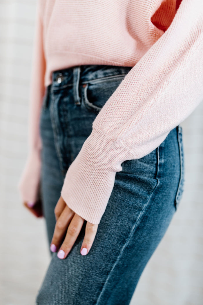 Pictured is a pink jersey pullover with a plush knit material, cuffed sleeves, cropped body, and v-neckline.