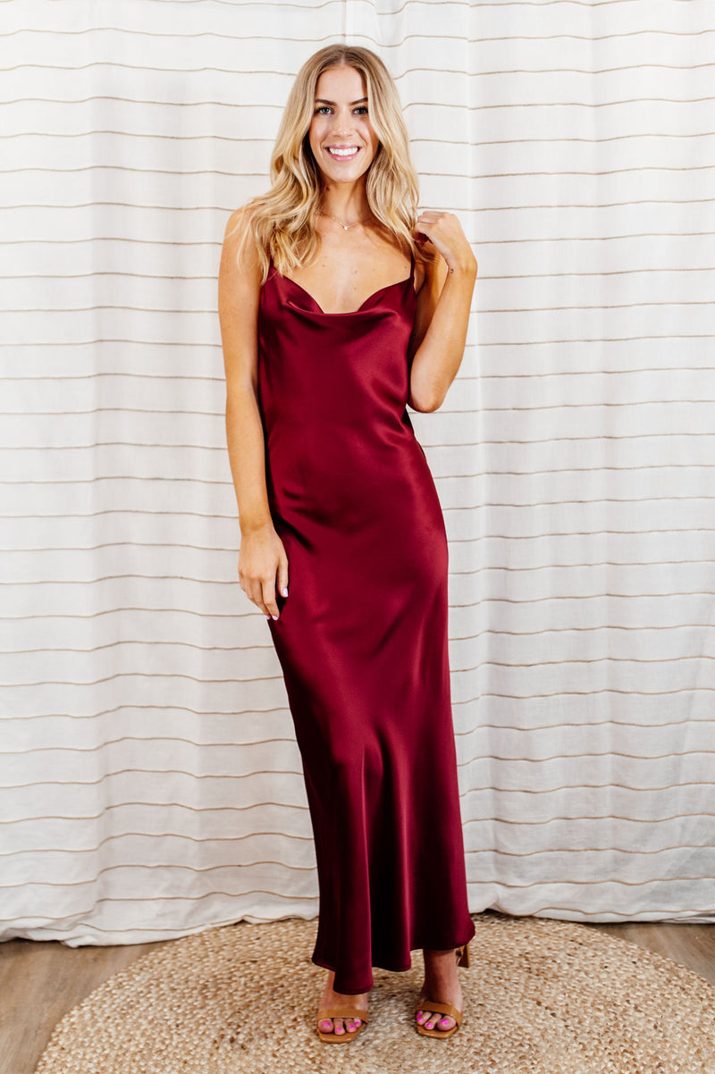 Pictured is a red, silky maxi dress with a cowl neckline, adjustable shoulder straps, and a low back. 