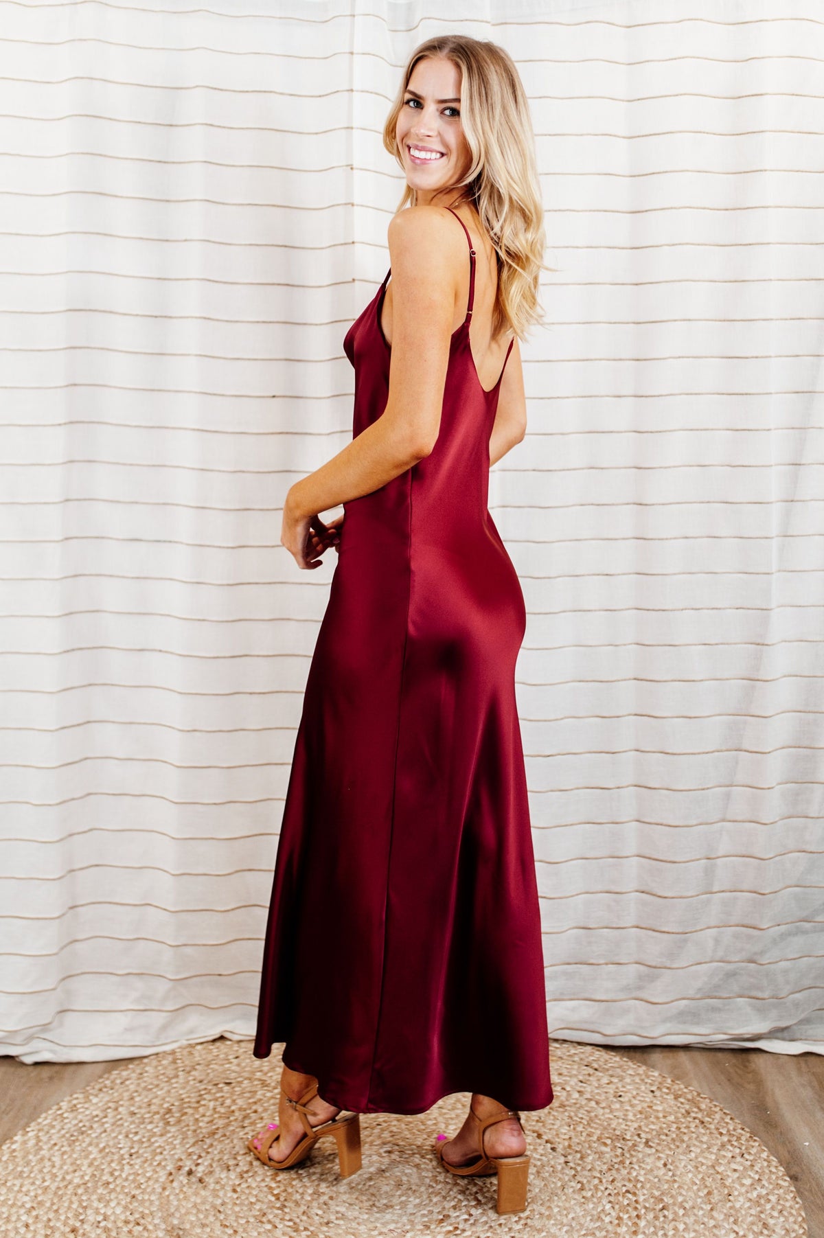 Pictured is a red, silky maxi dress with a cowl neckline, adjustable shoulder straps, and a low back. 