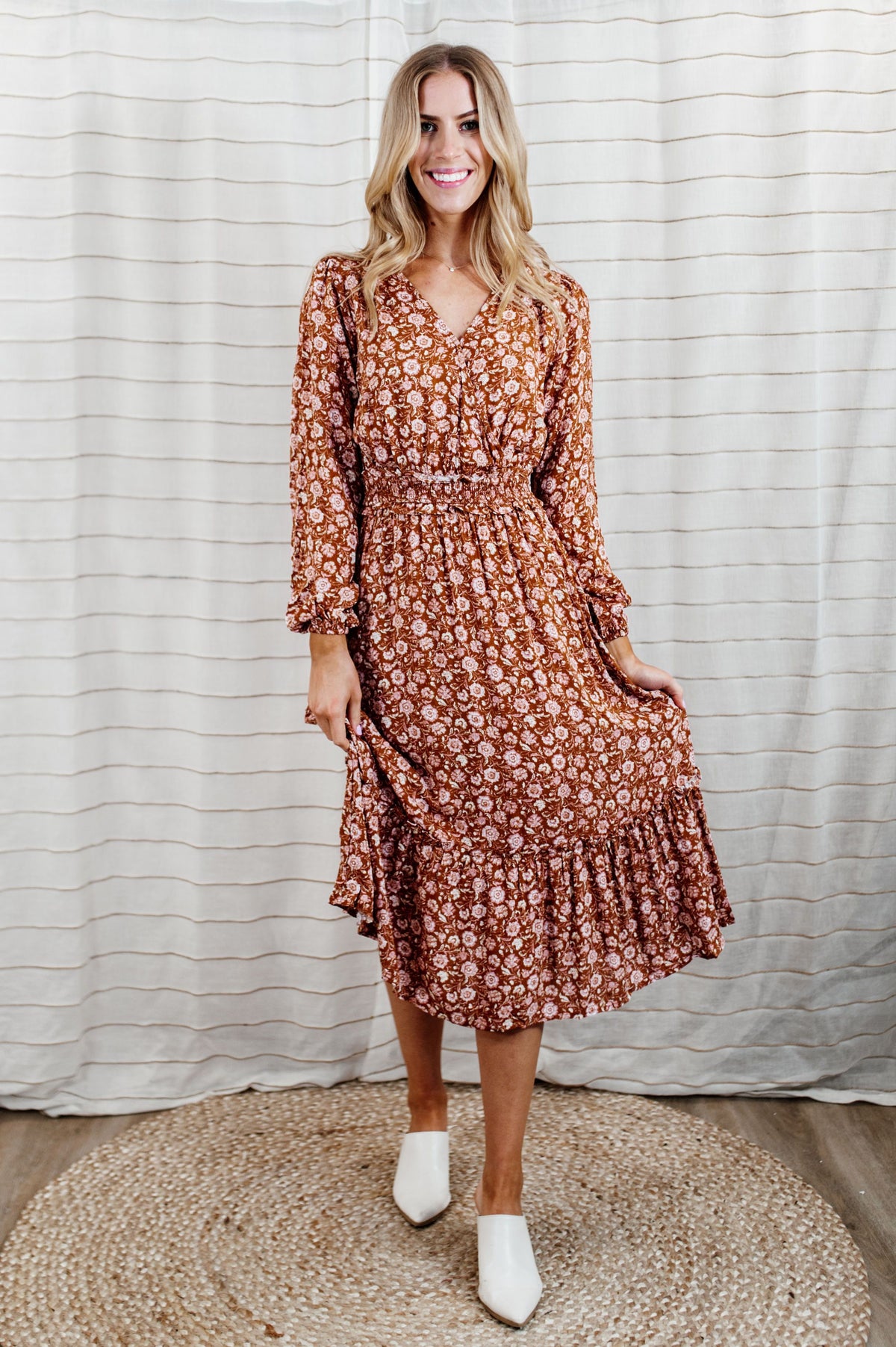 Pictured is a burnt-orange, long sleeve midi dress with a v-neckline, wrap style bust, ruffled waistline and detailing, and flowy long sleeves. 