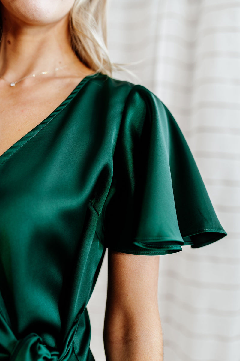 Pictured is a green, silky wrap dress with flowy sleeves and a wrap style body. 