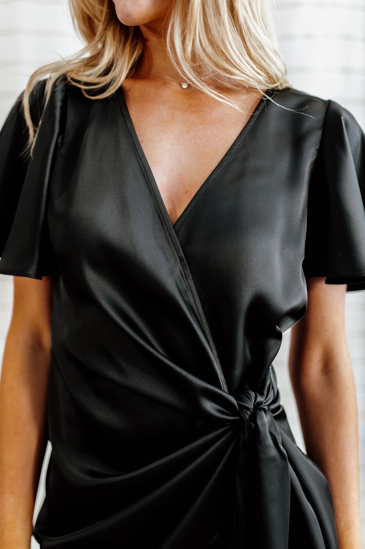 Pictured is a black, silky wrap dress with flowy sleeves and a wrap style body. 