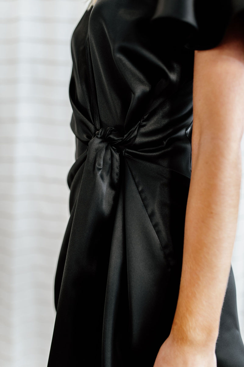 Pictured is a black, silky wrap dress with flowy sleeves and a wrap style body. 