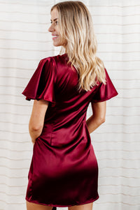 Pictured is a red, silky wrap dress with flowy sleeves and a wrap style body. 